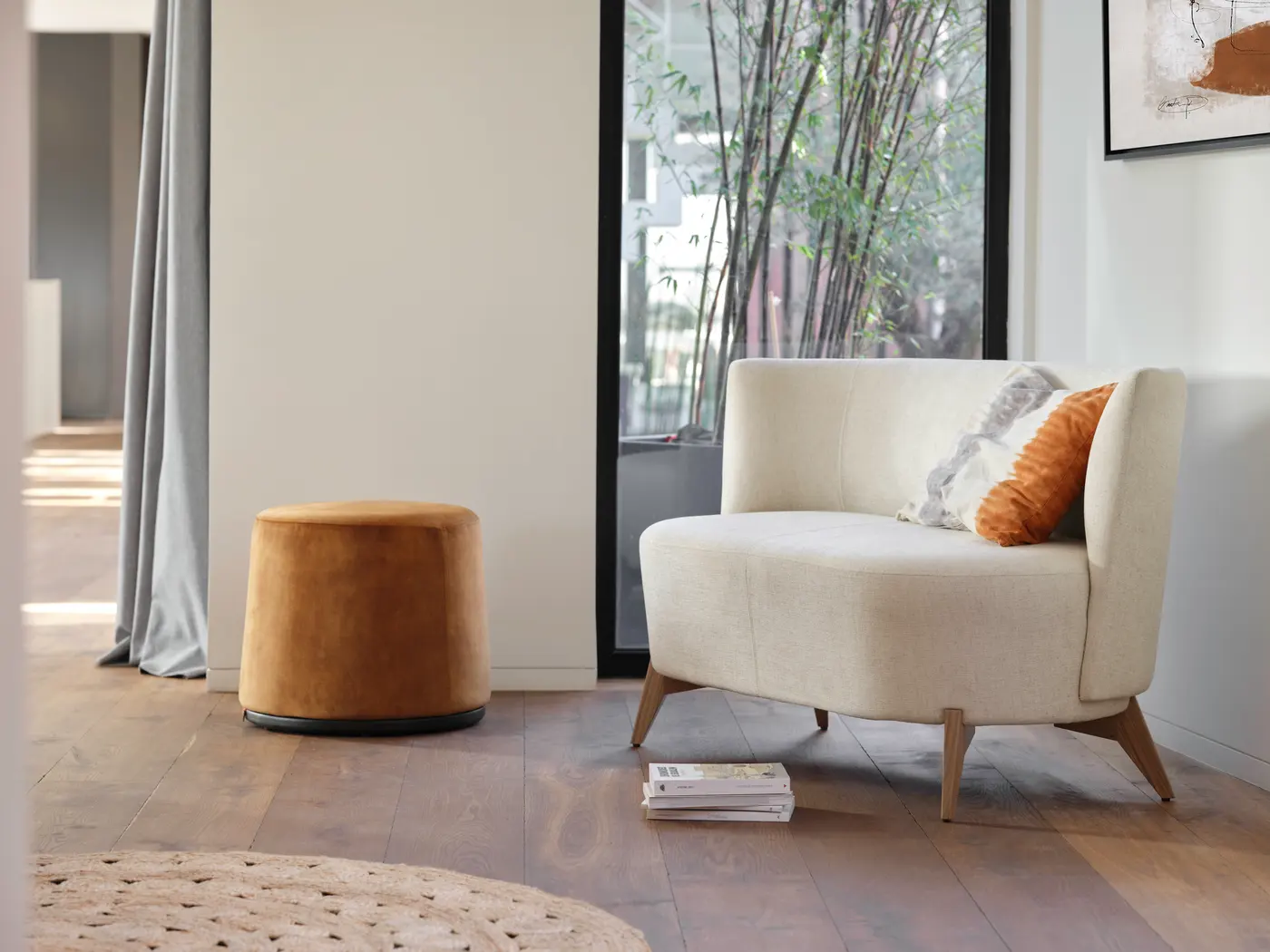 Canapé clair près d’une fenêtre, table basse et pouf.
