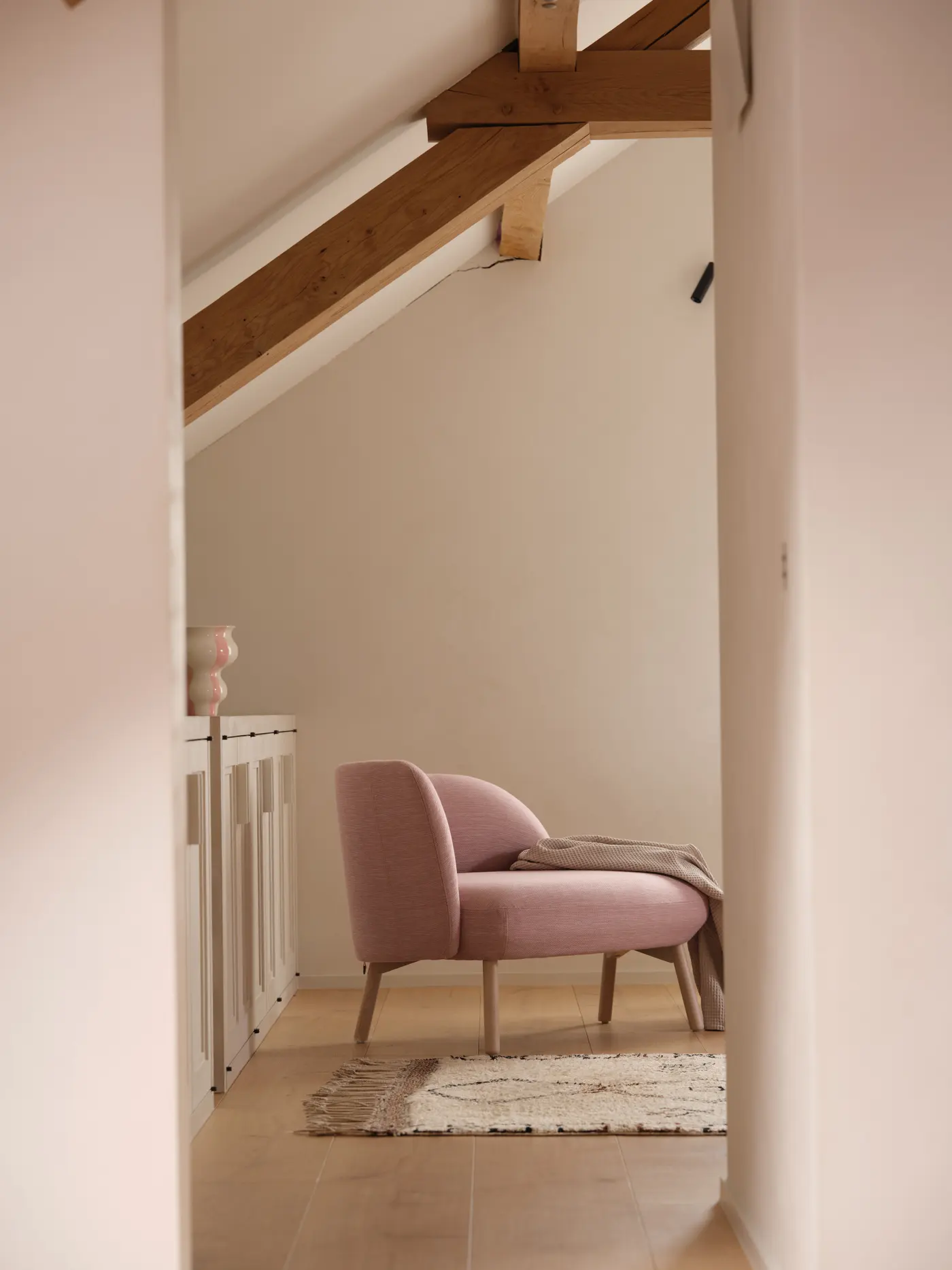 Fauteuil rose sous une poutre, dans un coin clair.