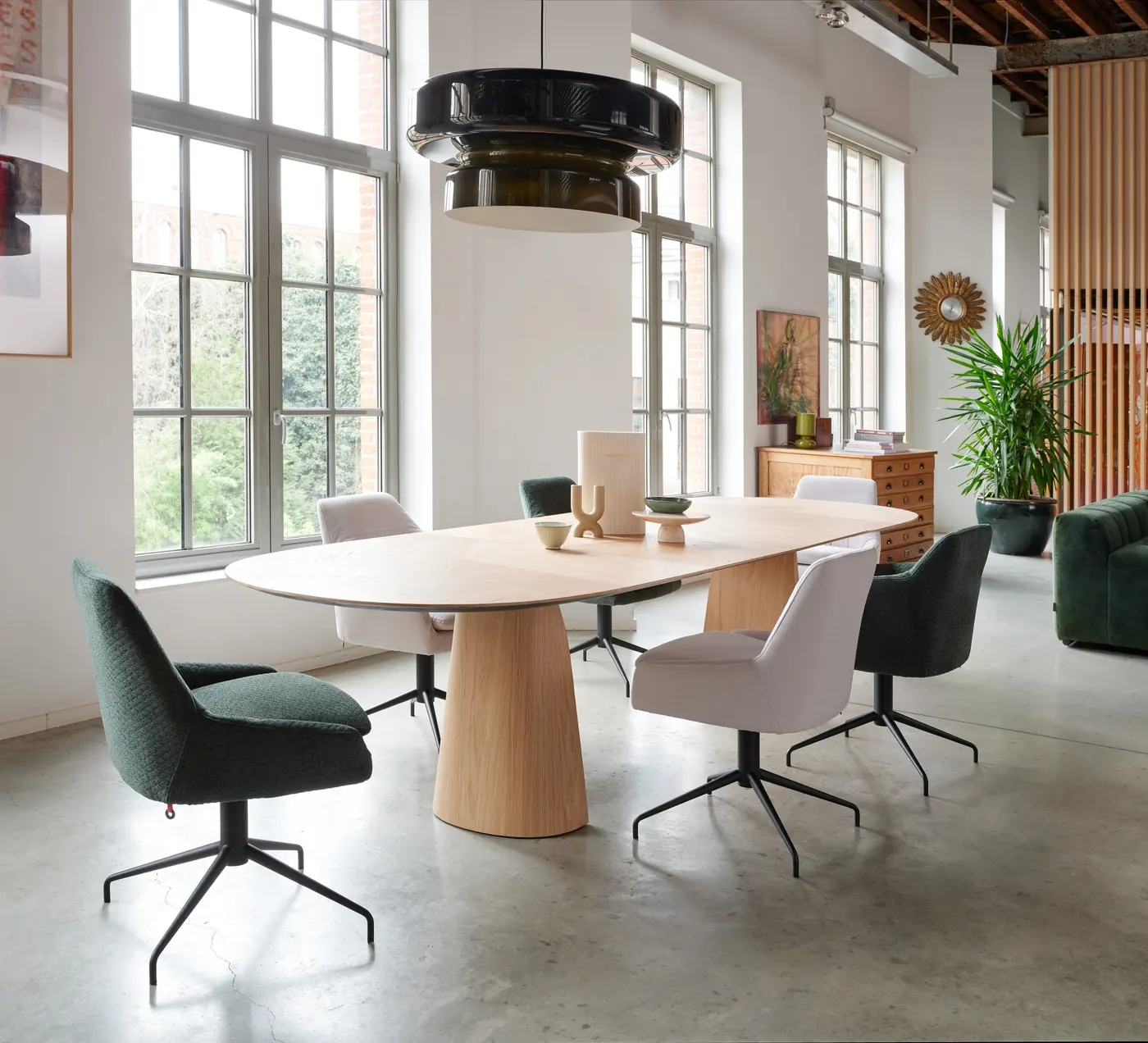 Grande salle claire, table en bois et sièges textiles, sous de hautes fenêtres.