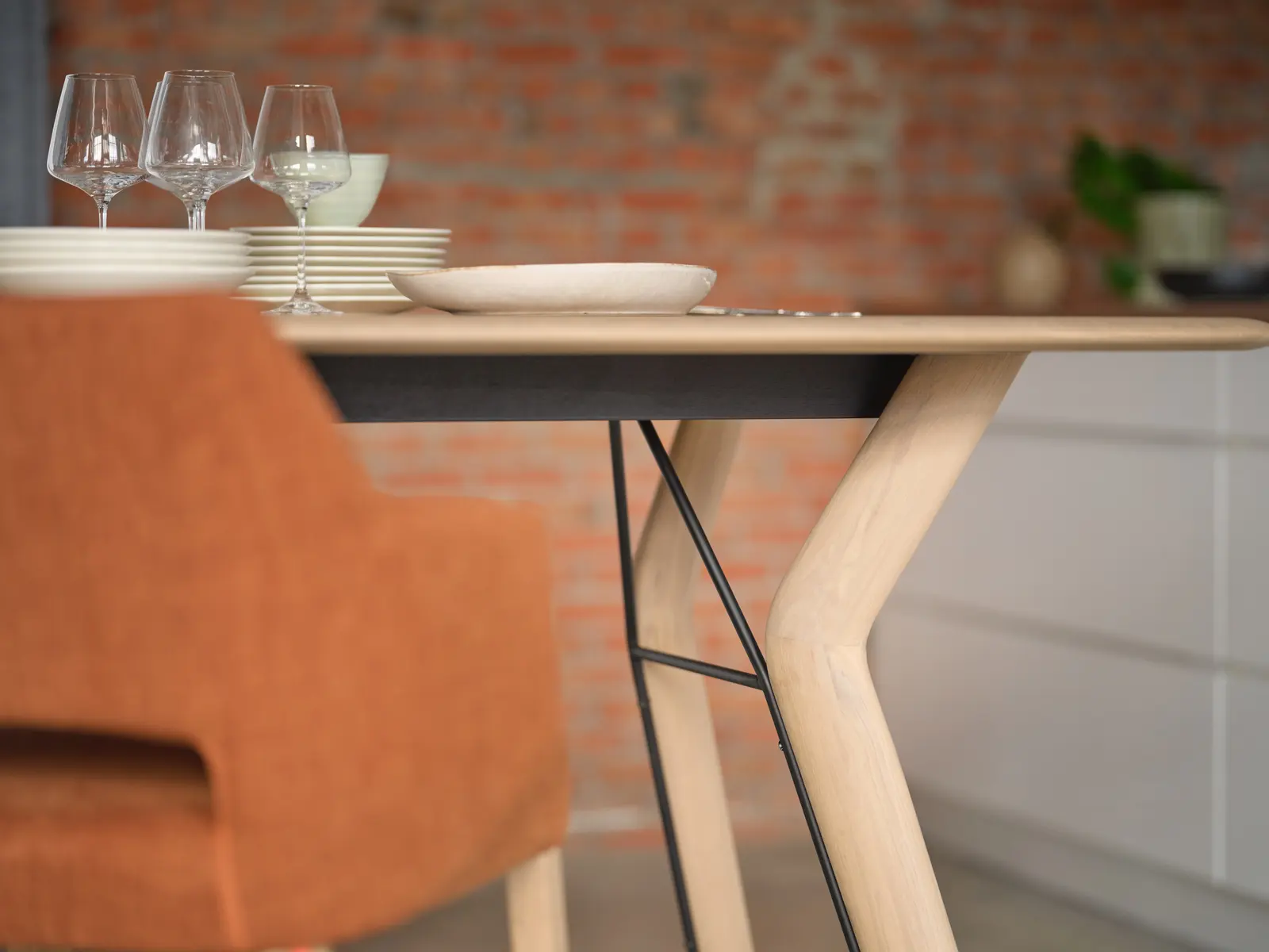 Table en bois clair dressée, chaise terracotta et mur de brique.